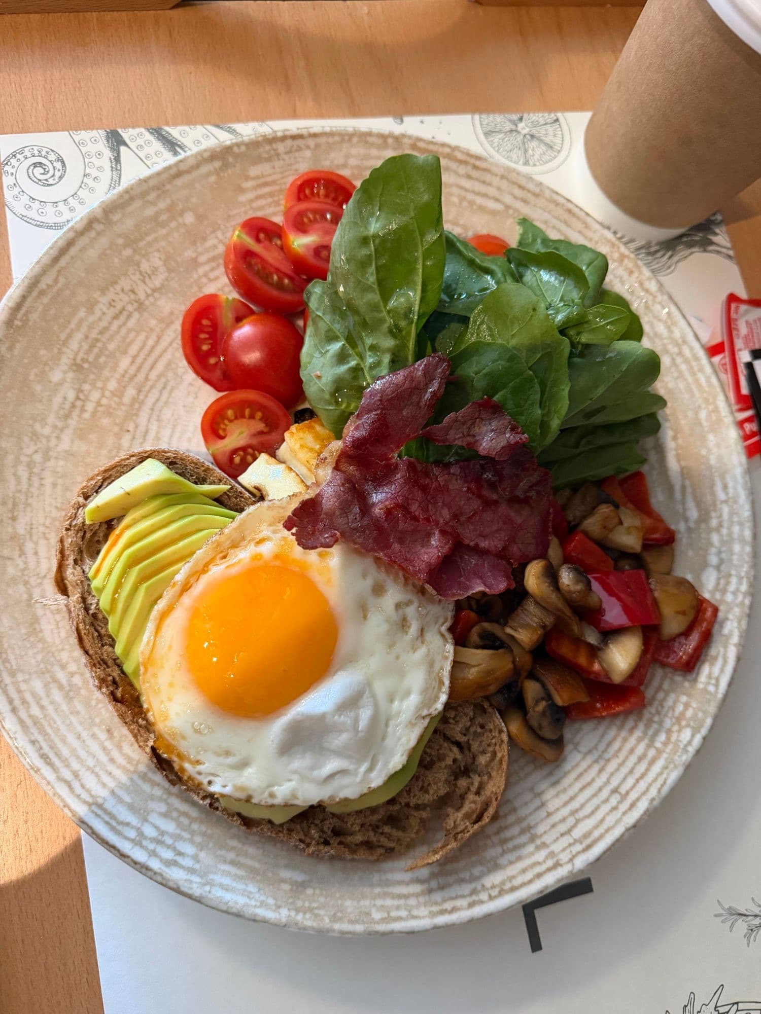 Avocado toast with a fried egg, pastrami, greens, tomatoes, and sautéed mushrooms and peppers.
