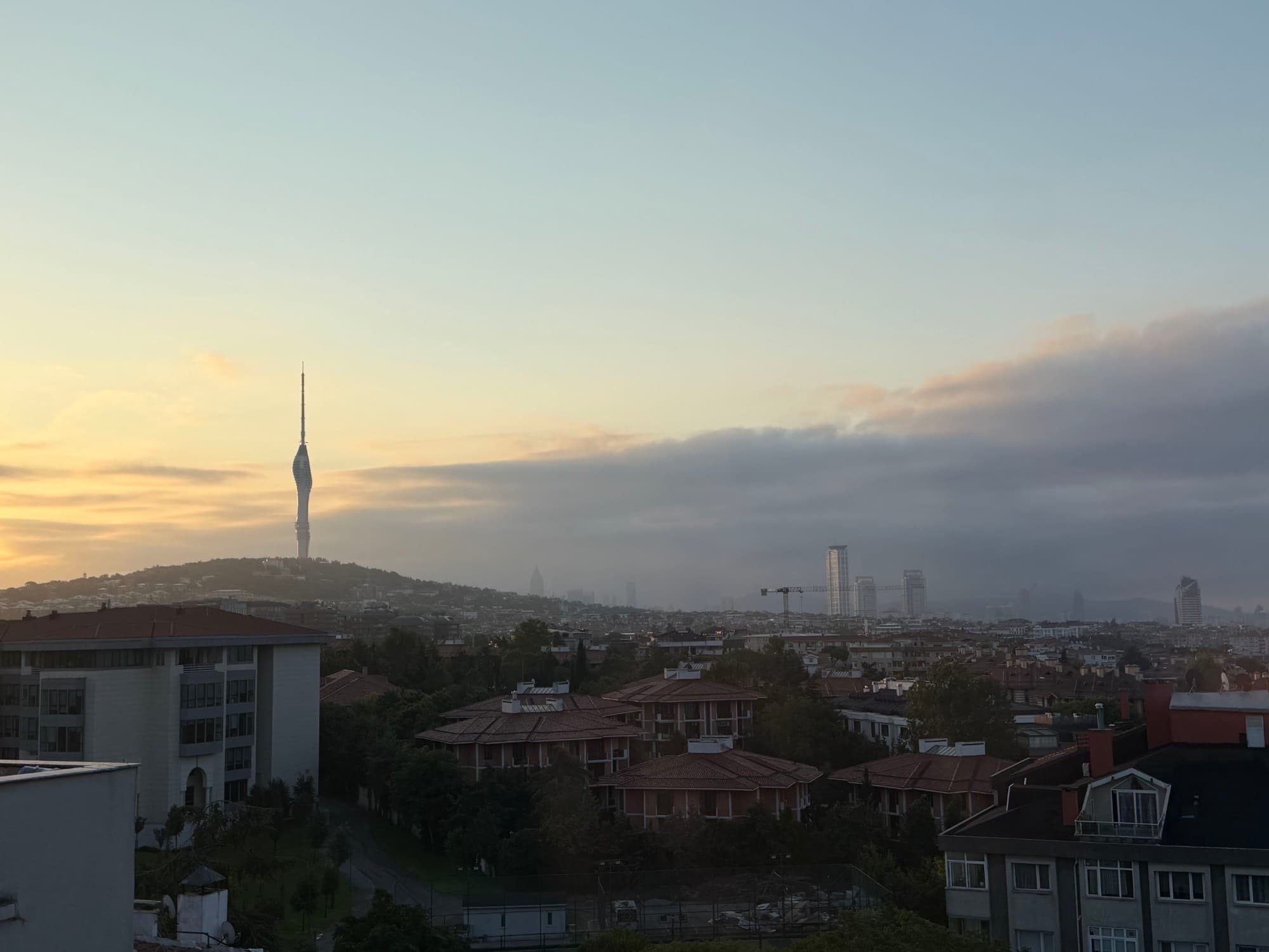 Sunrise over Istanbul rooftops, with Çamlıca Tower on a hill and low clouds over the skyline.
