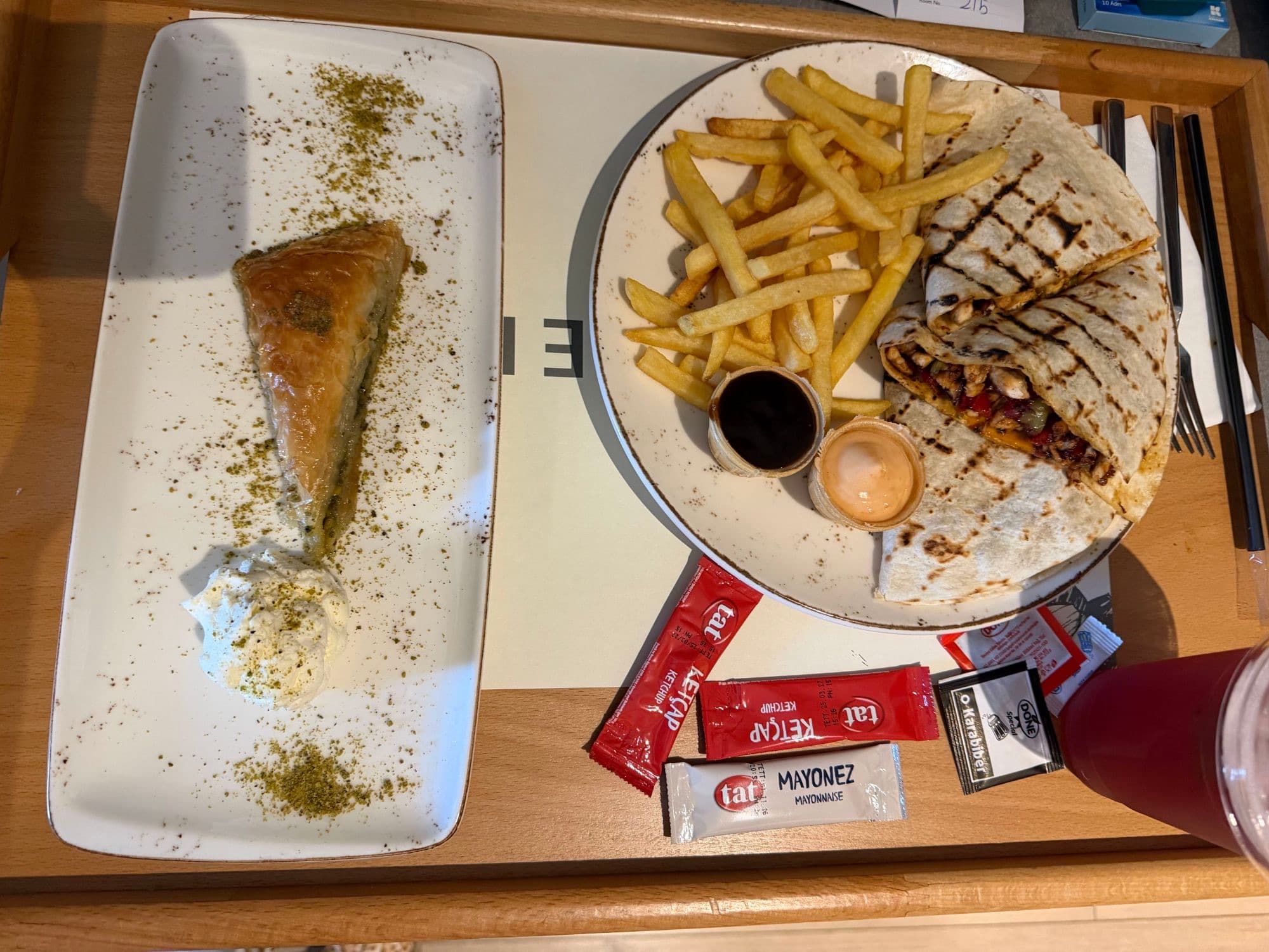 A tray with a grilled chicken wrap, fries, and a slice of pistachio baklava with cream.